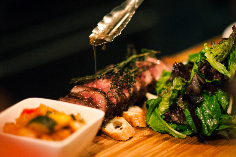 A wooden cutting board with some meat and vegetables on it